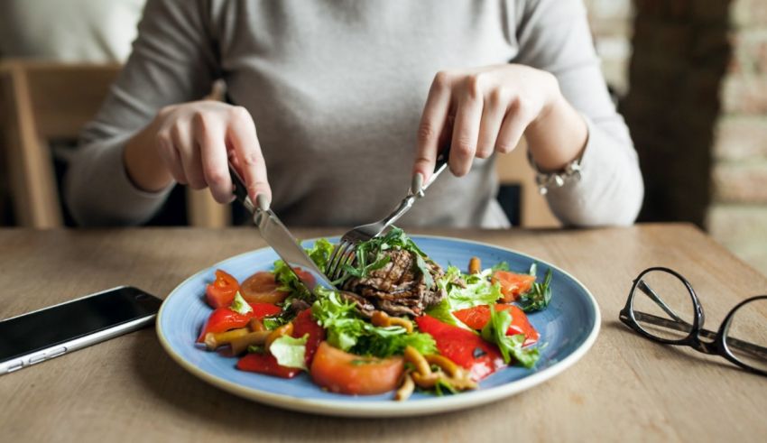 A woman is eating a salad with a fork and a cell phone.