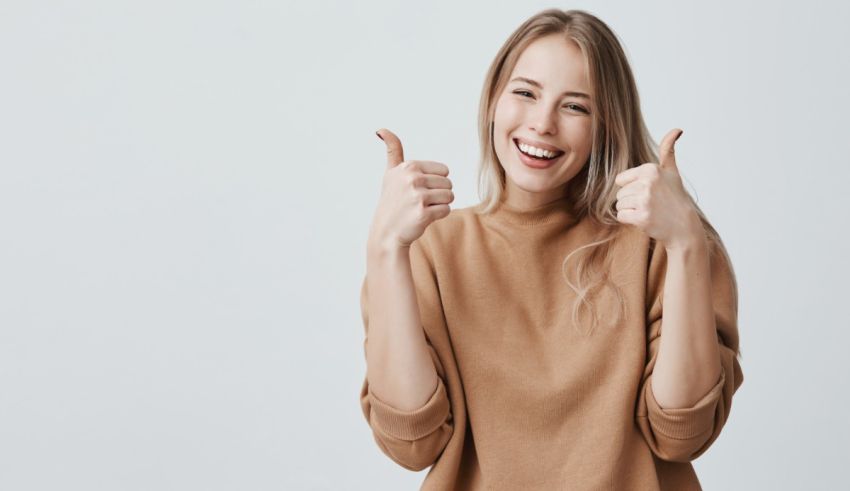 A young woman giving a thumbs up on a gray background.