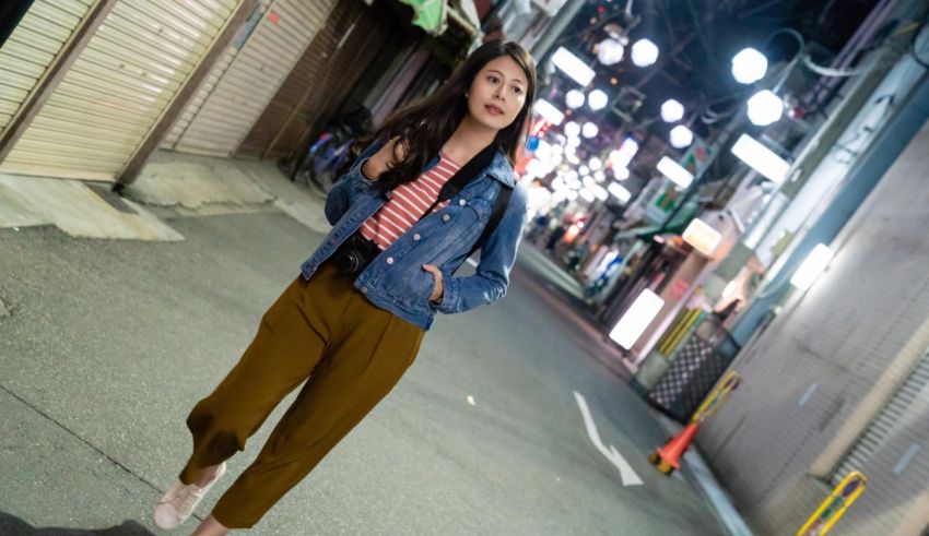 A woman in a denim jacket walking down a street at night.