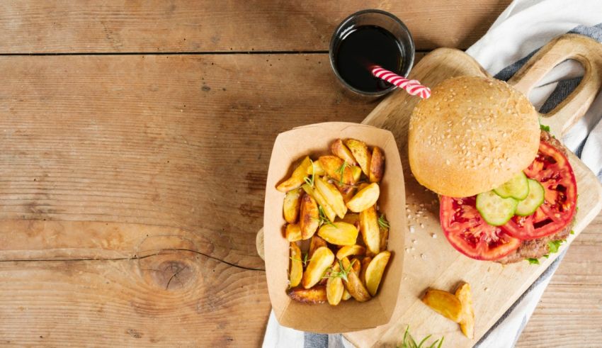 A burger with fries and a bottle of wine on a wooden table.