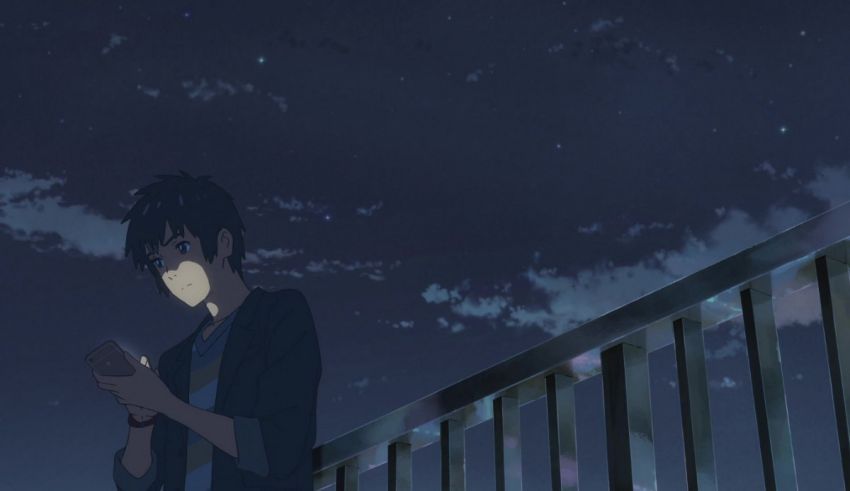 A boy is standing on a railing looking at his phone.