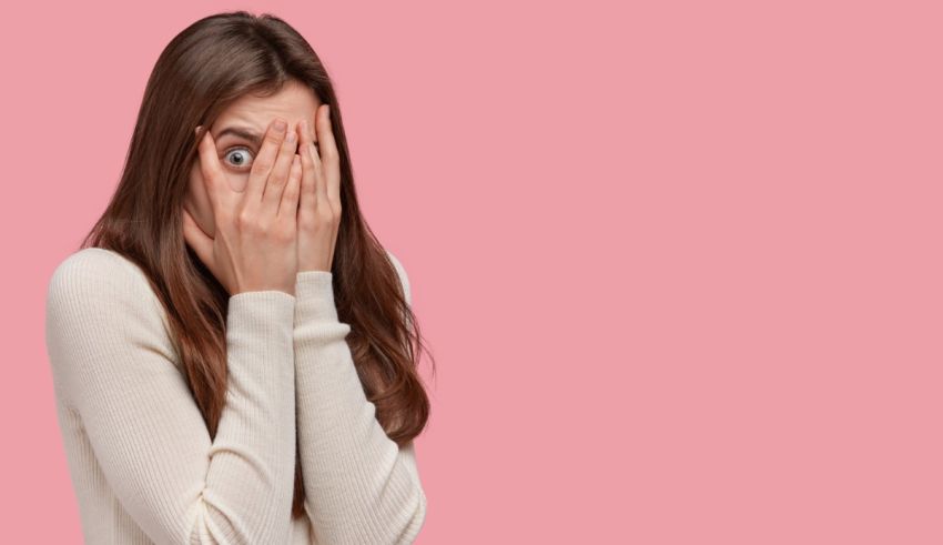A woman covering her eyes with her hands on a pink background.