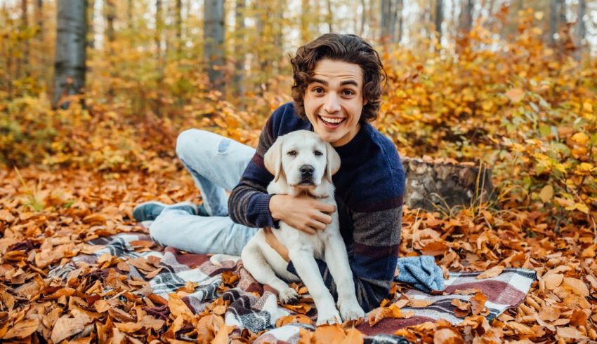 A young man sitting on a blanket with his dog in the woods.
