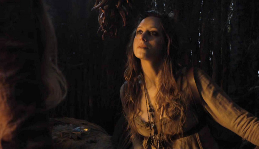 A woman with long hair is standing in a wooded area.