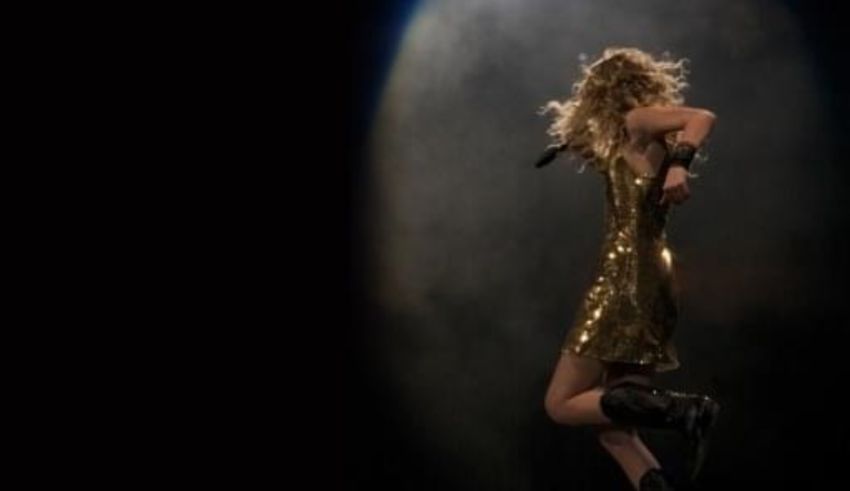 Taylor swift performs on stage in a gold dress.