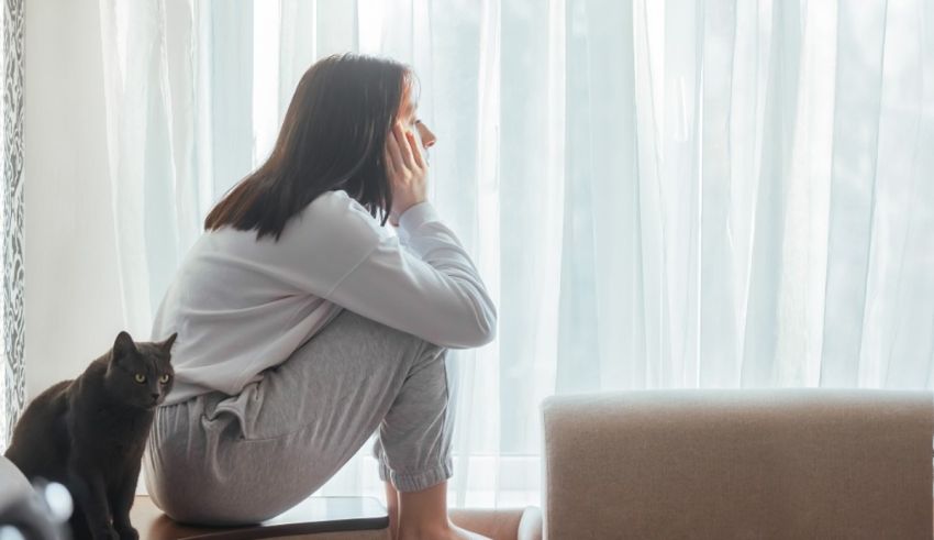 A woman sits on the floor next to a cat.