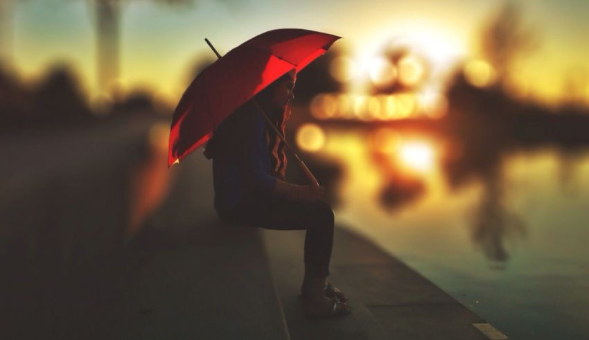 A woman sitting on a ledge with a red umbrella.