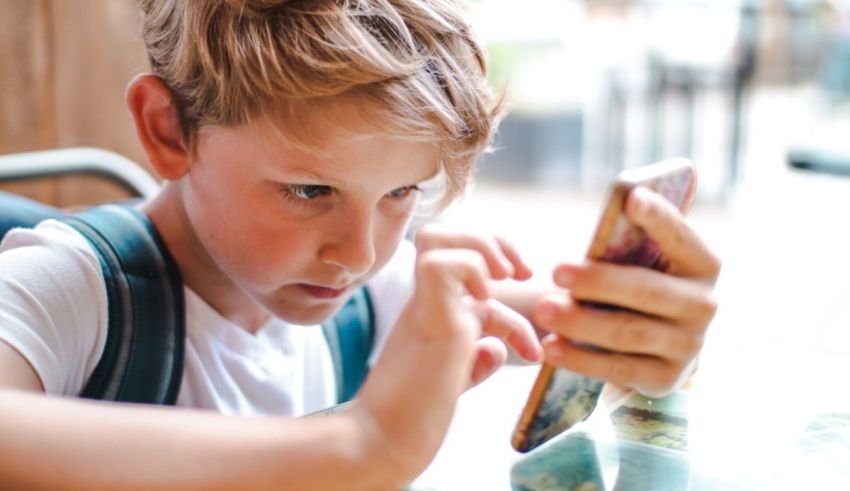 A young boy looking at a cell phone while sitting at a table.