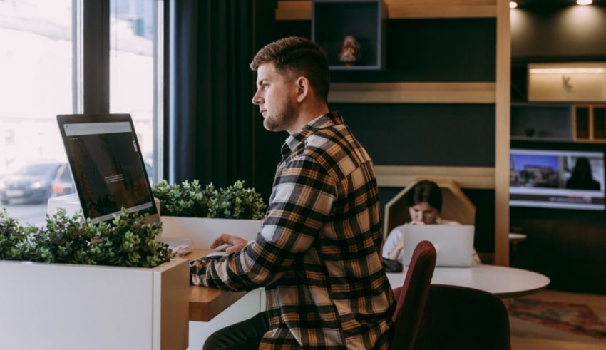 A man sitting at a desk with a laptop in front of a window.