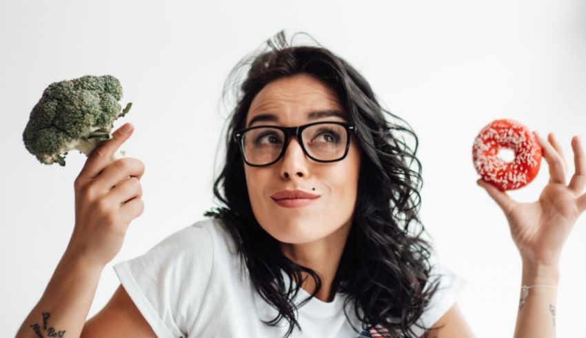 A woman with glasses holding broccoli and a donut.
