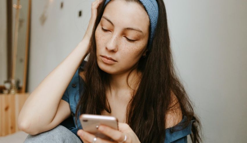 A young woman looking at her phone while sitting on the floor.