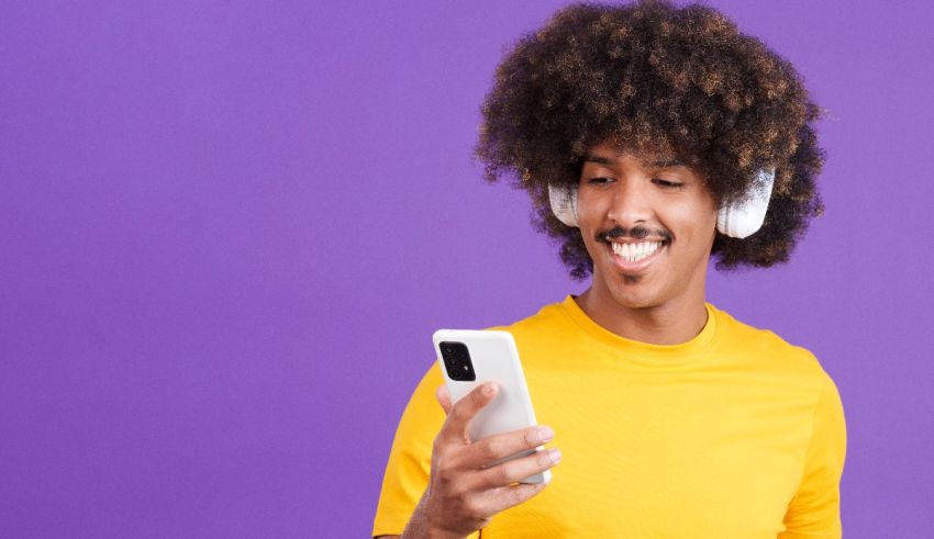 A young man with afro hair wearing headphones and listening to music on his phone.
