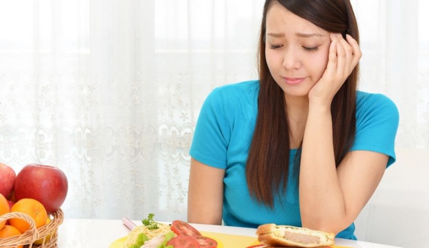 A woman is sitting at a table with a sandwich and vegetables.