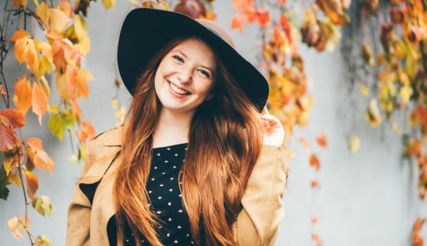 A young woman wearing a hat and polka dot dress in front of autumn leaves.