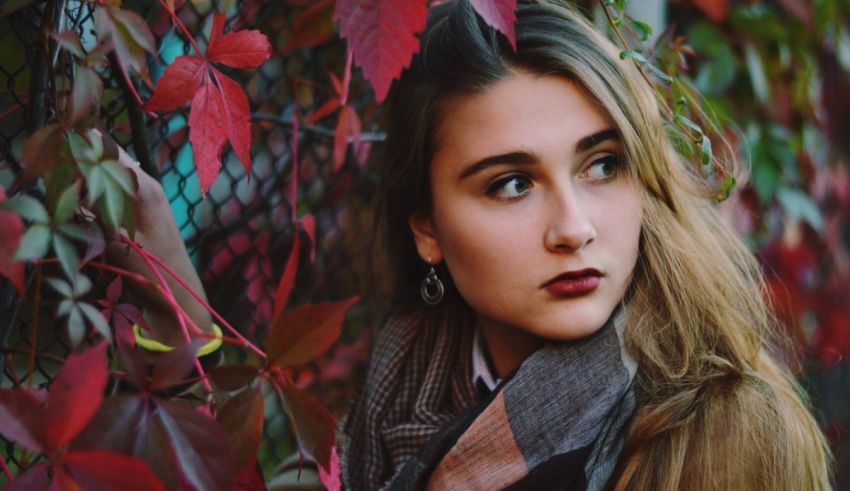 A girl is leaning against a fence with red leaves.