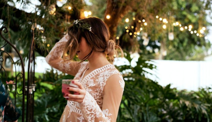 A woman is holding a drink in front of a tree.