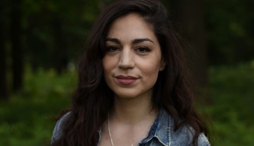 A woman in a denim shirt is standing in the woods.