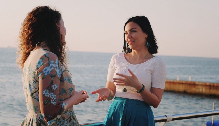 Two women talking on a balcony overlooking the sea.