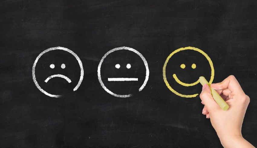 A hand drawing three smiley faces on a blackboard.