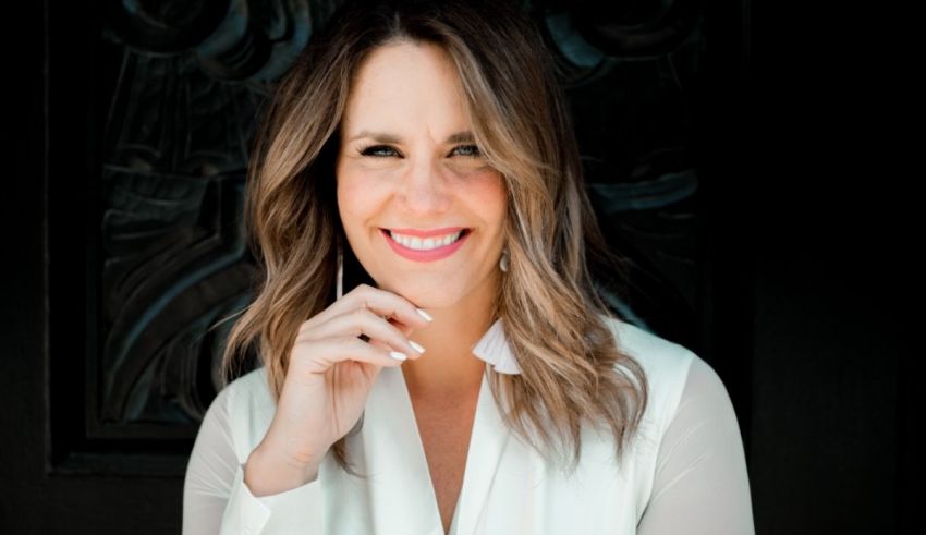 A woman in a white shirt smiling in front of a black door.