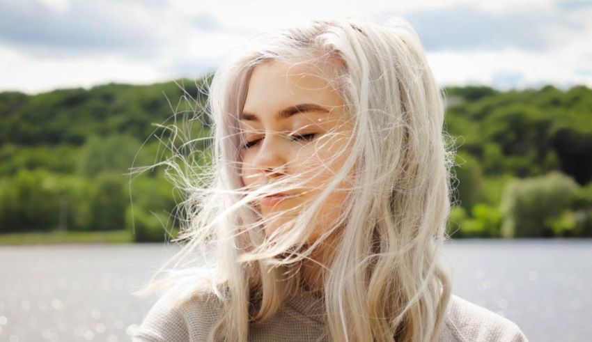 A young woman with long white hair standing by a lake.