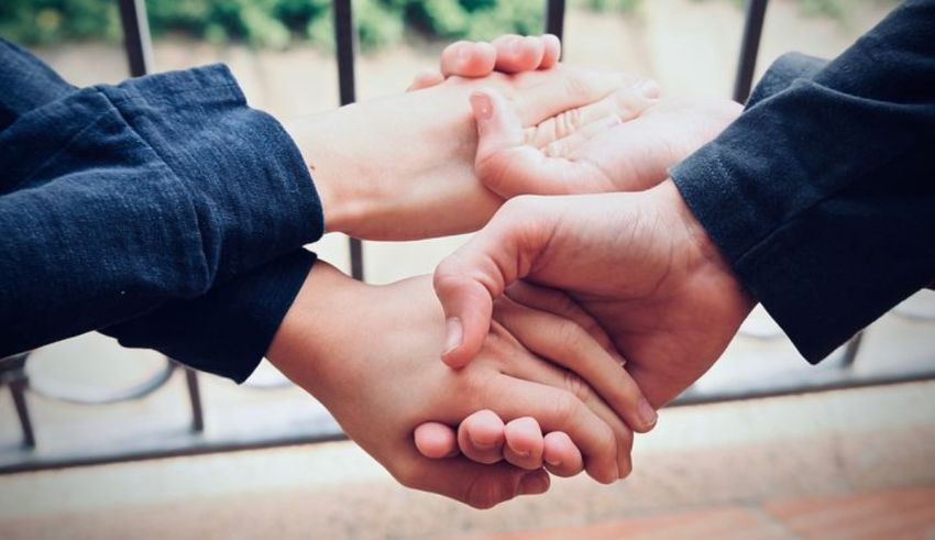 Two people holding hands in front of a fence.