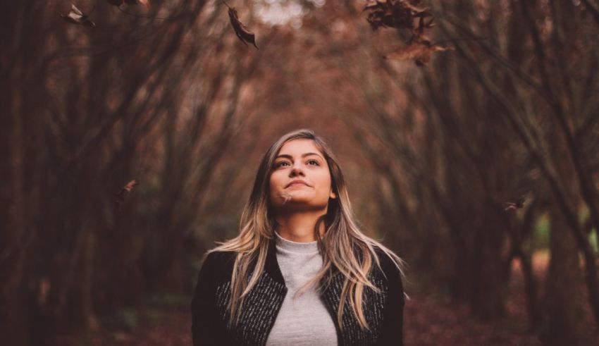 A woman standing in a forest with leaves falling around her.