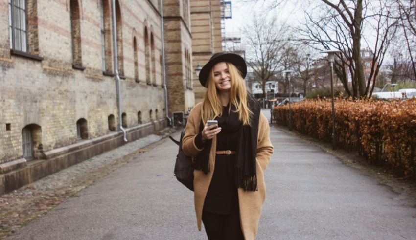 A woman walking down a street in a black coat and hat.