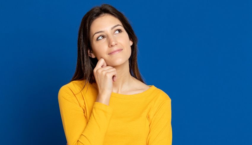 A young woman in a yellow shirt is looking at her hand and thinking.