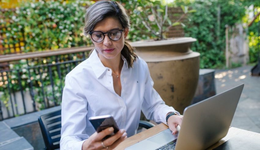 A woman is sitting at a table with a laptop and cell phone.