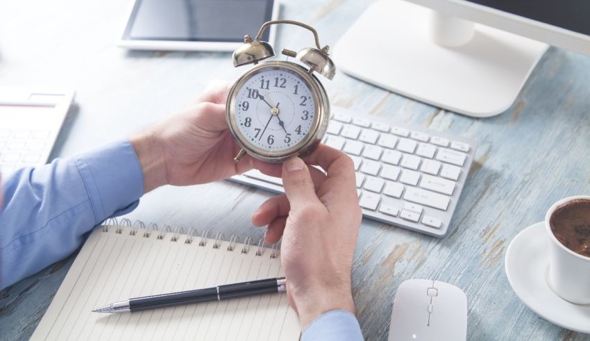 A person holding an alarm clock on a desk.