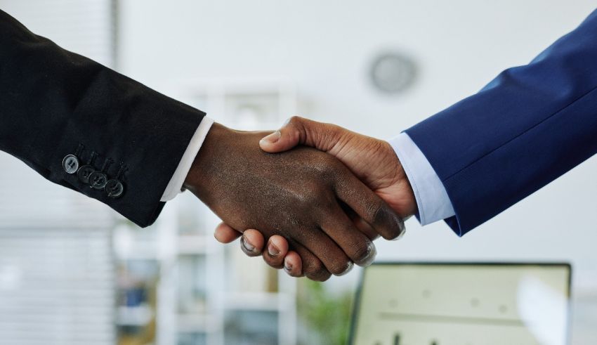 Two businessmen shaking hands in front of a computer.