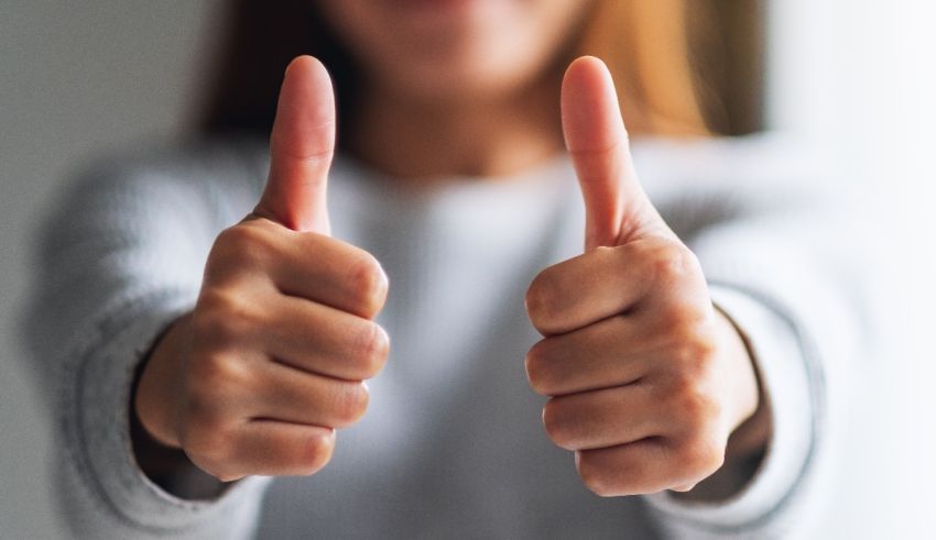 A woman showing her thumbs up in front of a window.
