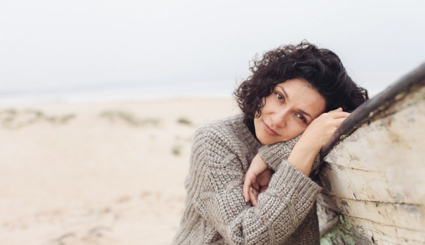 A woman leaning against a wooden boat on the beach.