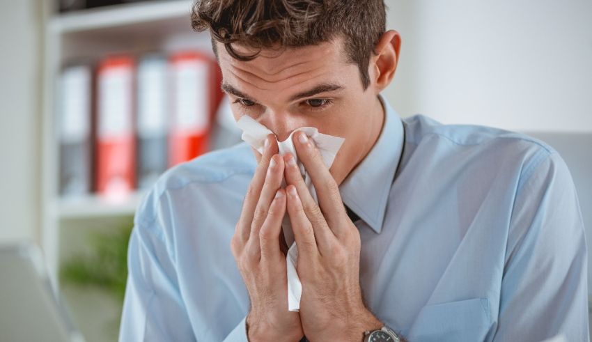 A man sneezing while sitting at his desk.
