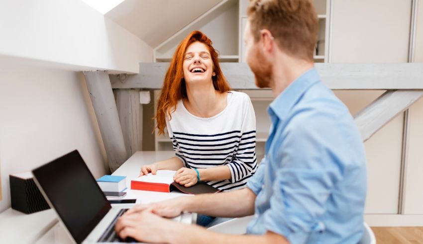 A man and woman sitting at a desk laughing.