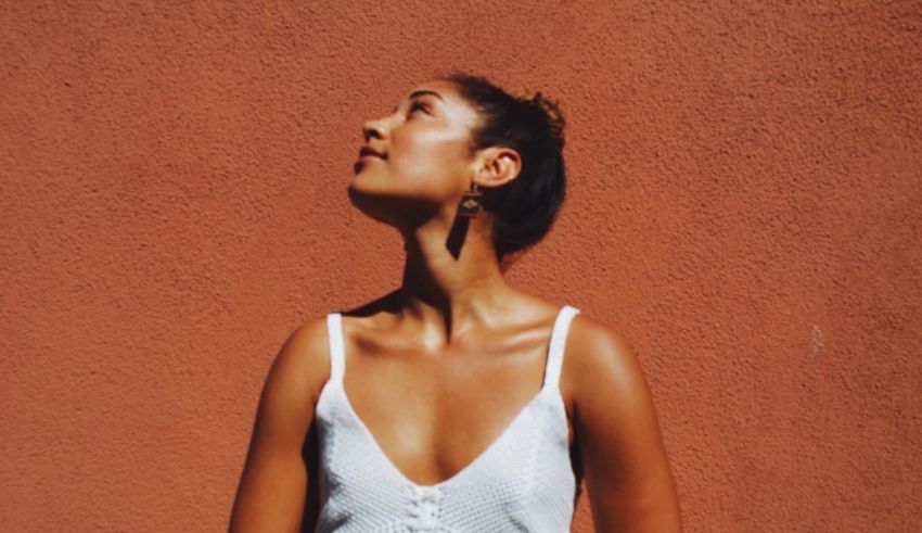 A woman in a white top is standing in front of a red wall.