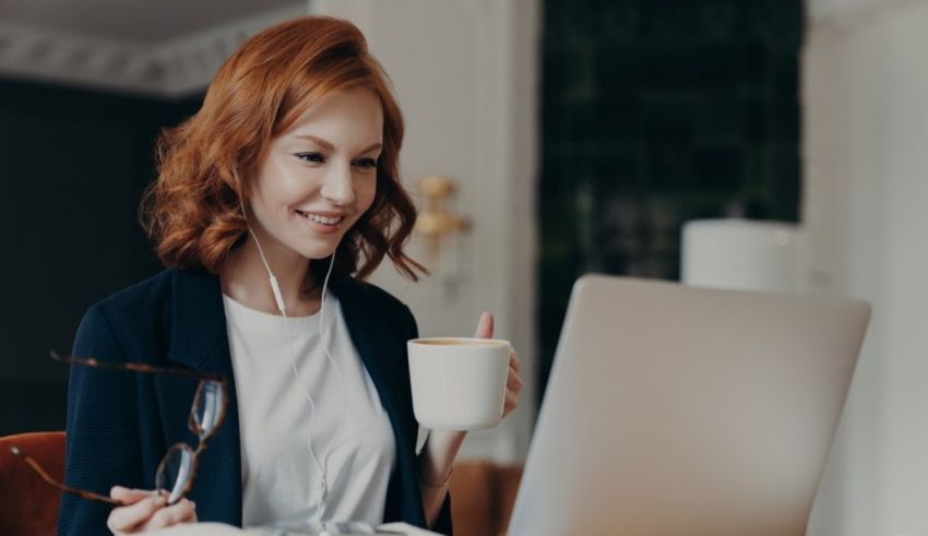 A woman with red hair sitting at a desk with a laptop and a cup of coffee.