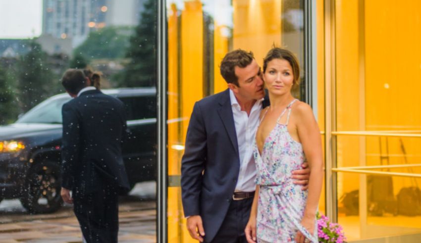 A couple kisses in front of a car in the rain.