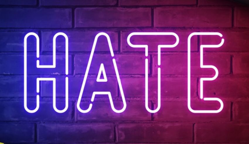 A neon sign with the word hate against a brick wall.