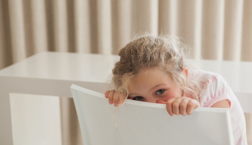 A little girl peeking over the edge of a white chair.