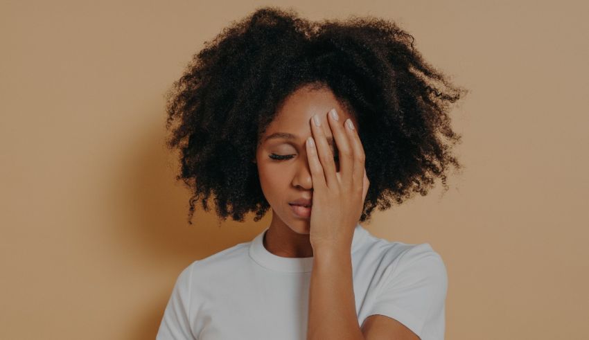 A woman with afro hair covering her face with her hands.