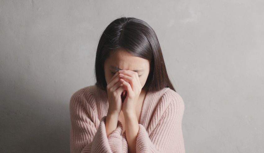 A young asian woman covering her face with her hands.