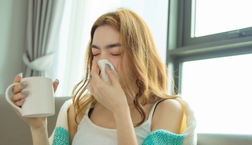 A woman blowing her nose while holding a cup of coffee.