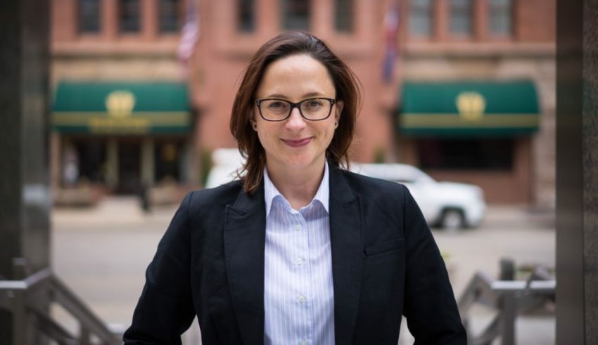 A woman in glasses is standing in front of a building.