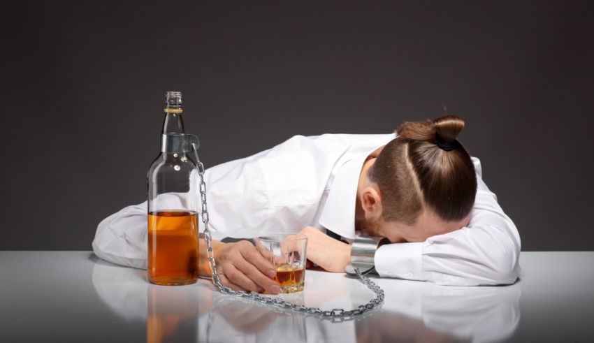 A man is chained to a table with a bottle of alcohol.