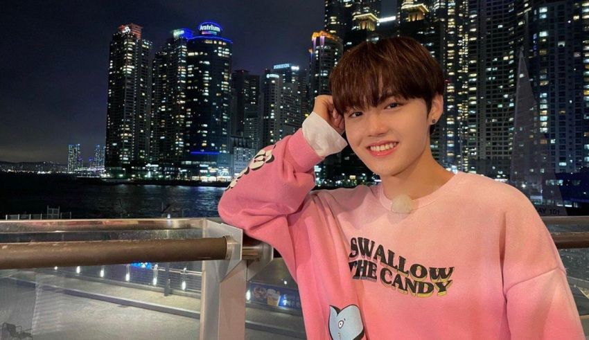 A young man in a pink sweatshirt standing on a balcony at night.