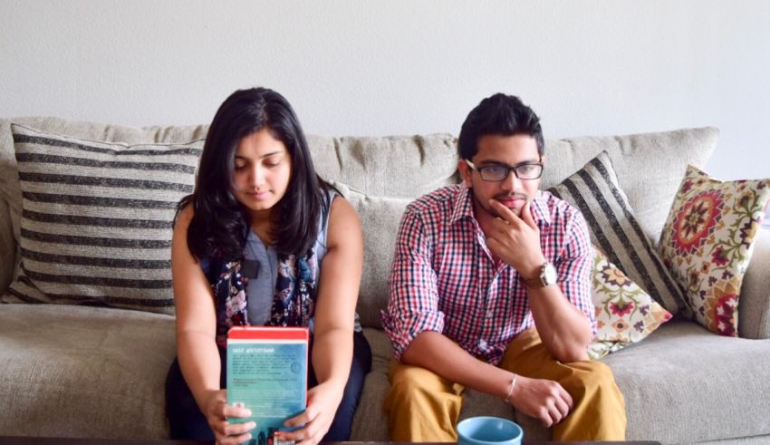 A man and woman sitting on a couch reading a book.