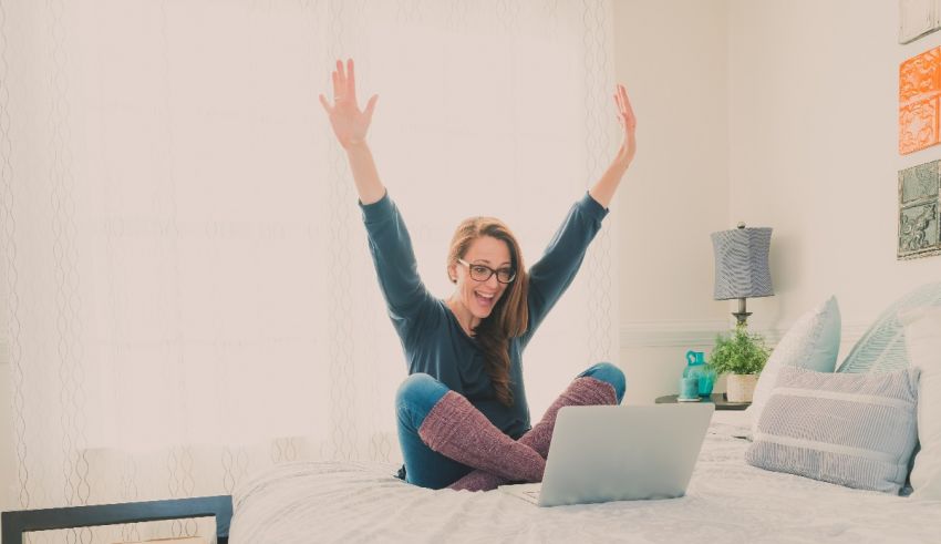 A woman is sitting on a bed with her arms raised.