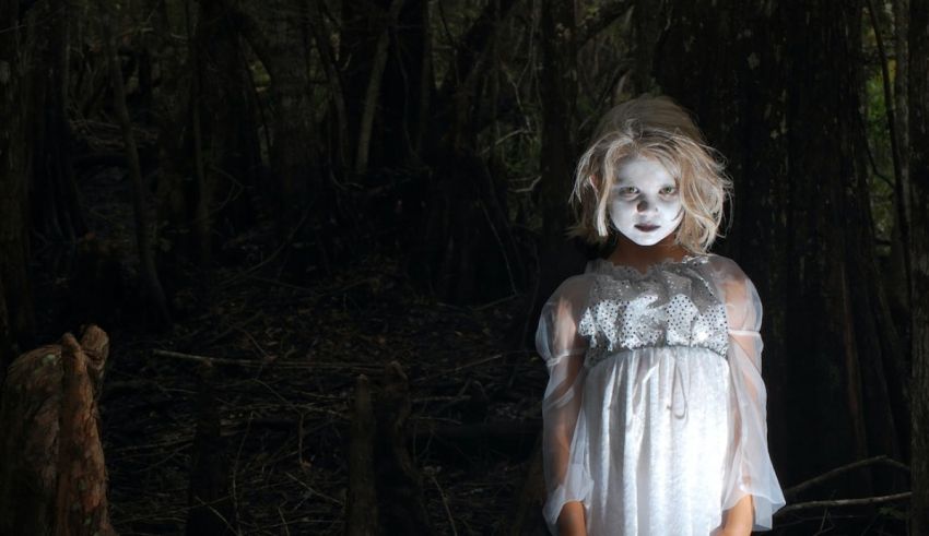 A girl in a white dress standing in the woods.
